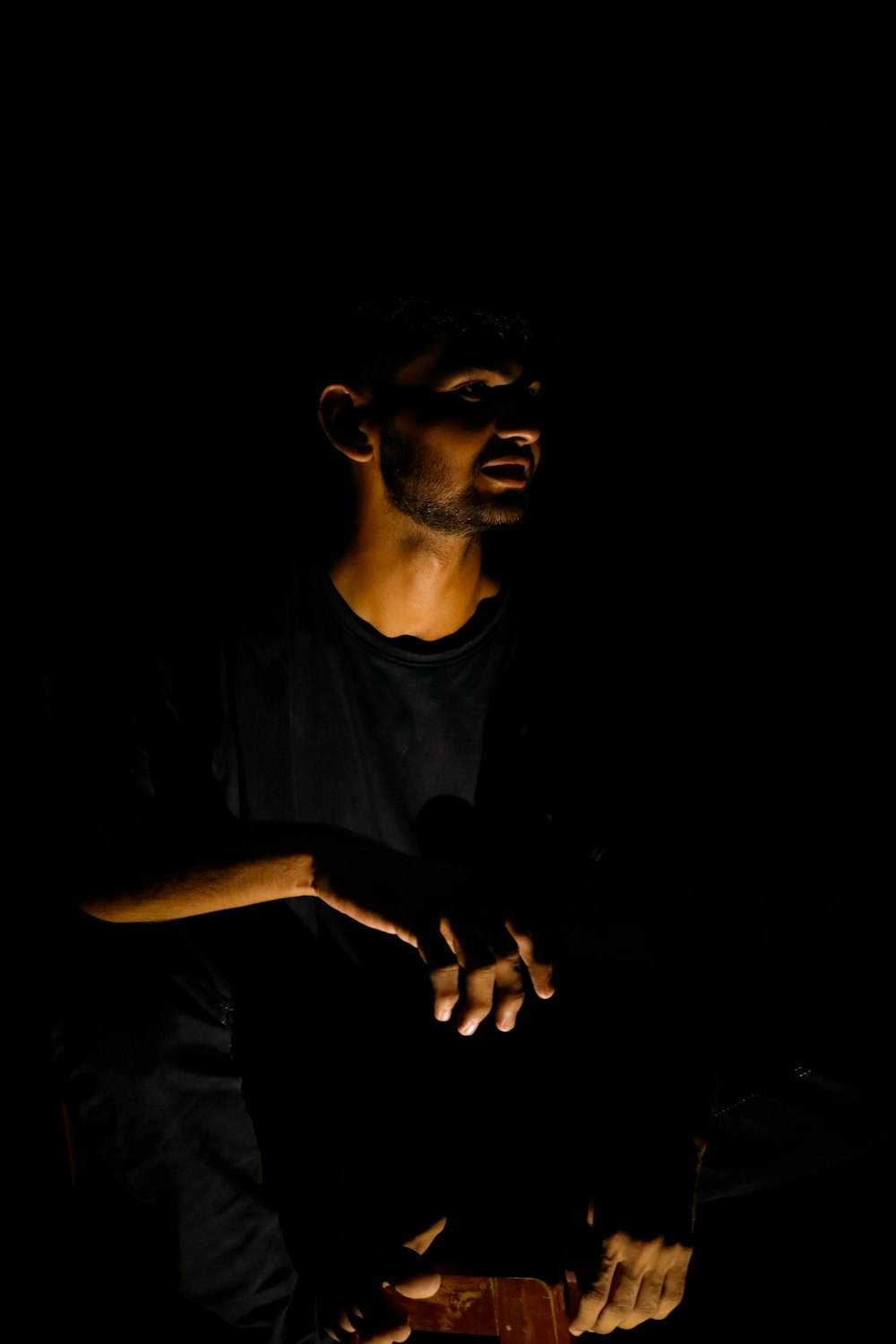 um homem sentado no escuro segurando um telefone celular