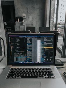 A modern office workspace with a laptop displaying code and data analytics charts.
