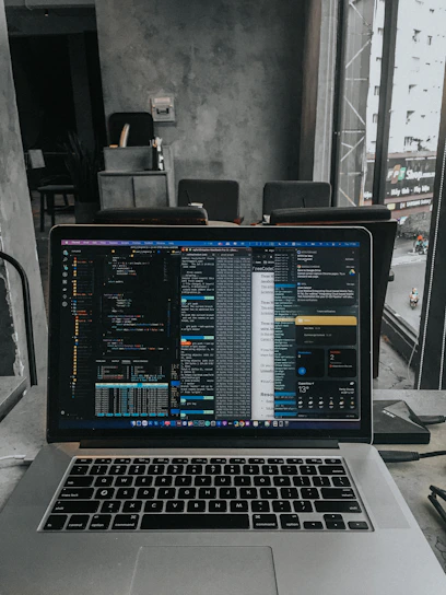 Modern office workspace with a developer coding on a laptop and multiple screens showing various software applications.