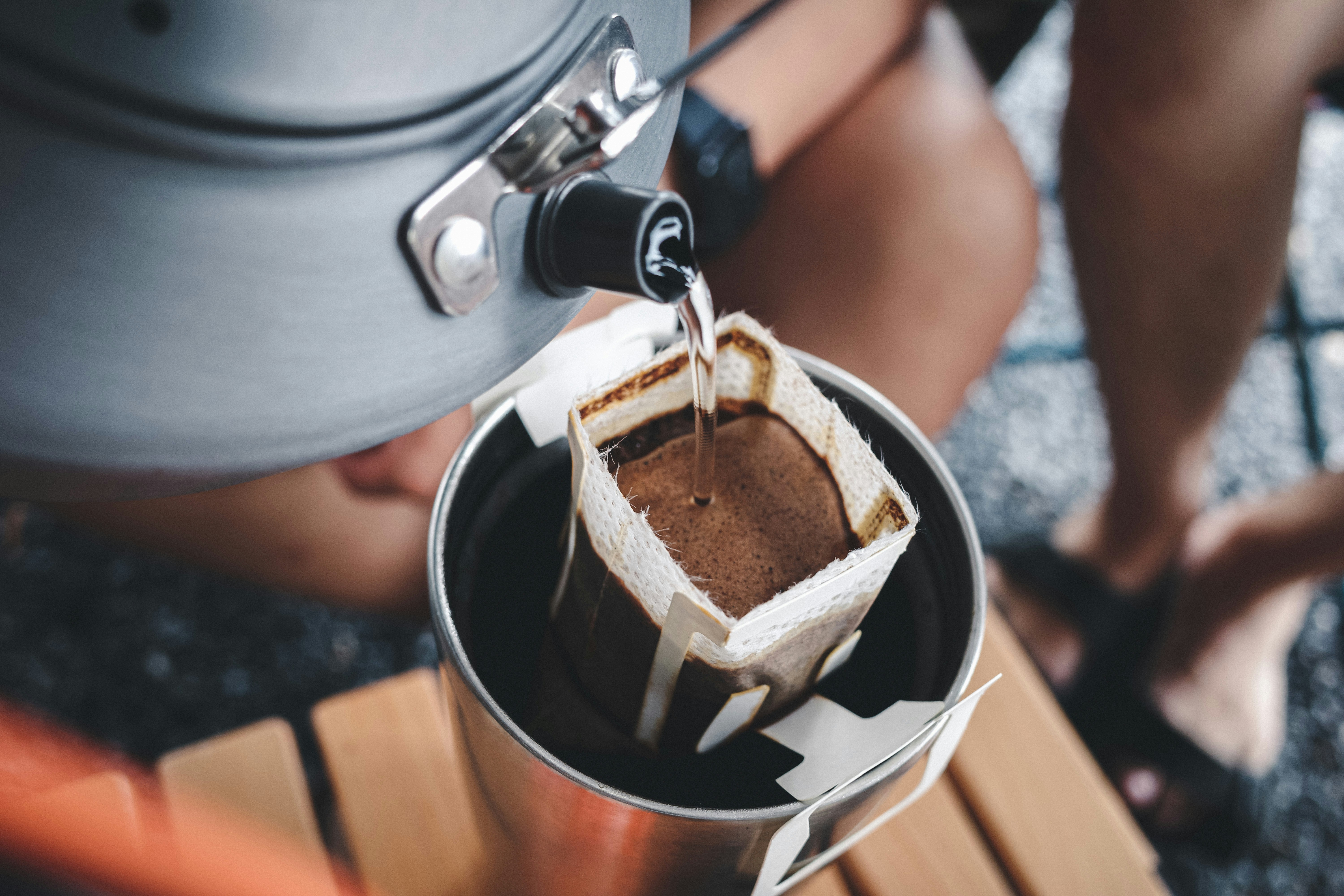 person brewing coffee with a portable brewer at a campsite picnic table