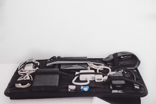 An organized grid containing various electronic accessories, including cables, a mouse, a power bank, and chargers, all secured with elastic bands.