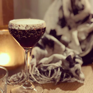A close-up of amber-hued cocktail swirling in a matte black glass, set against exposed brick and soft candlelight.