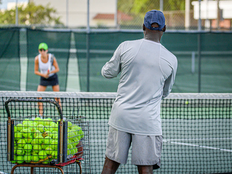 Entrenador con cesta de bolas dando una clase individual de tenis