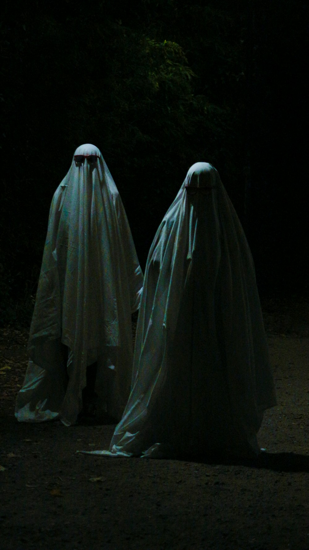 two ghostly people in white cloths walking in the dark