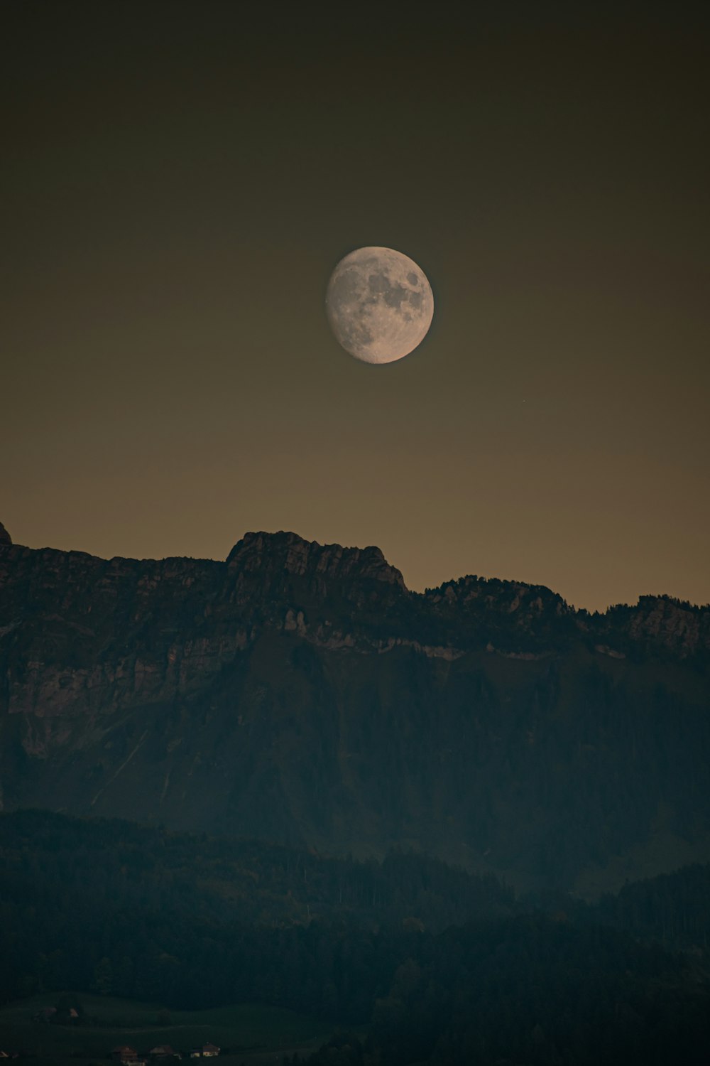 a full moon rising over a mountain range