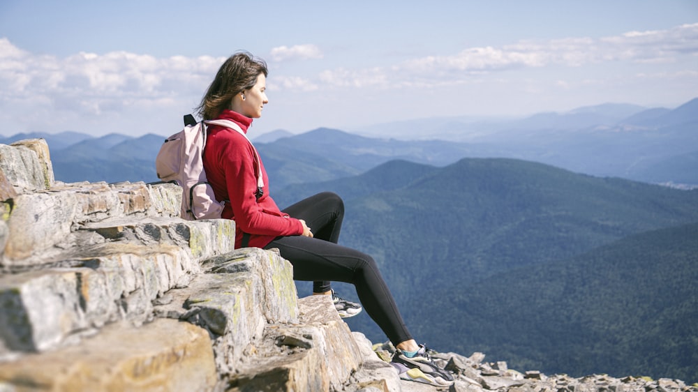 uma mulher sentada no topo de um penhasco de rocha