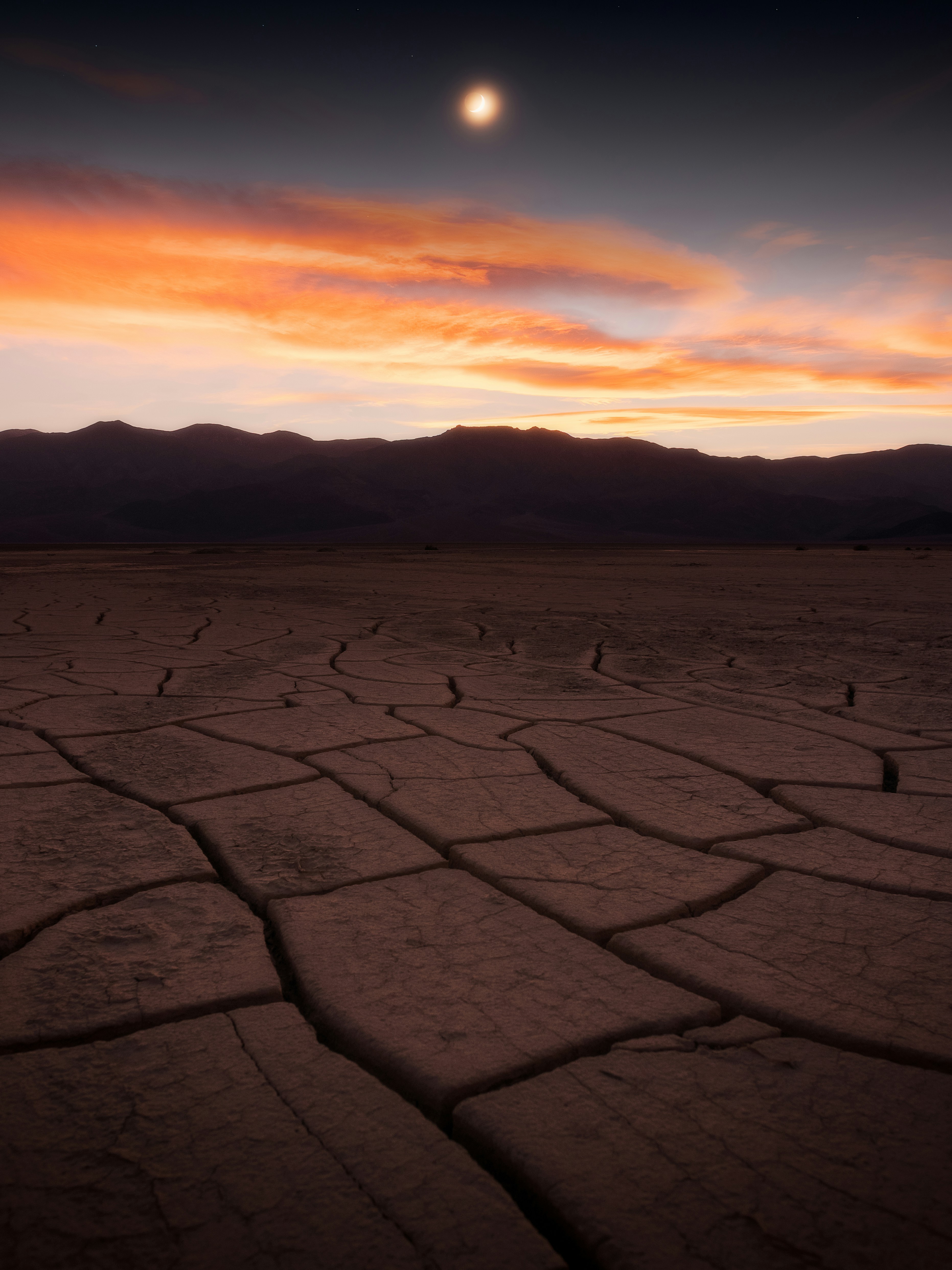 Paysage de terre fissurée sous un ciel dramatique au coucher du soleil.