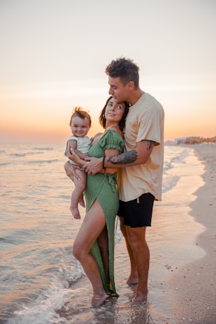 a man and woman holding a baby on the beach