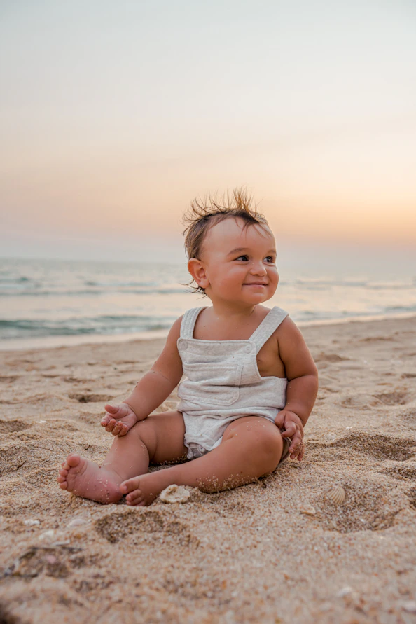 a baby sitting in the sand at the beach