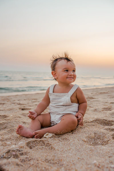 a baby sitting in the sand at the beach