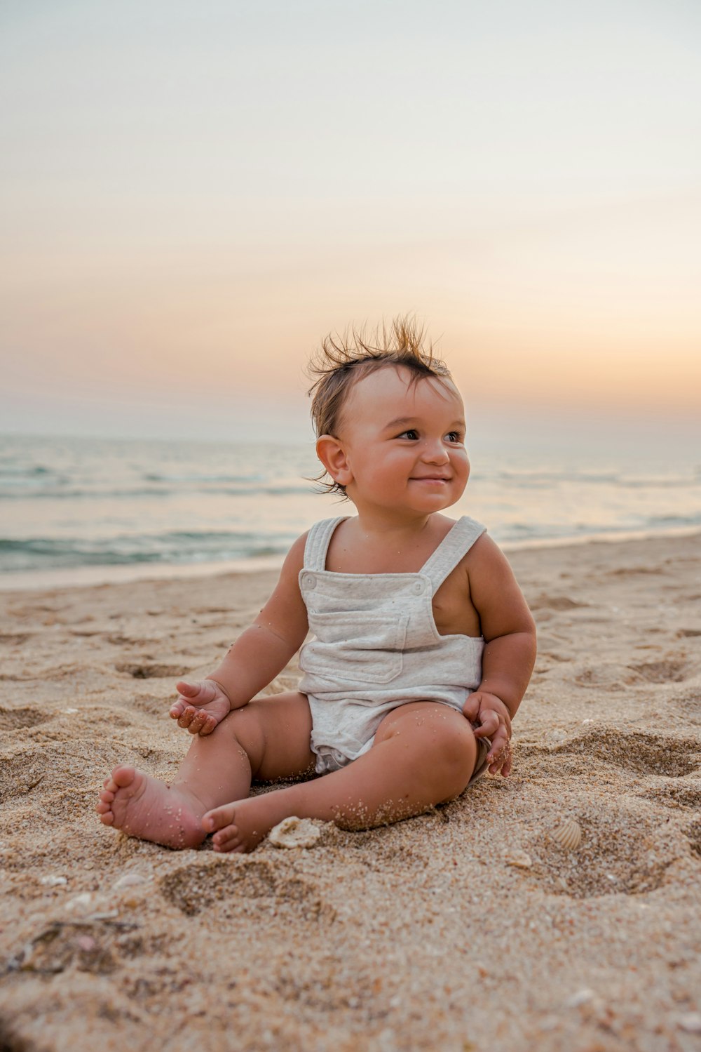 a baby sitting in the sand at the beach