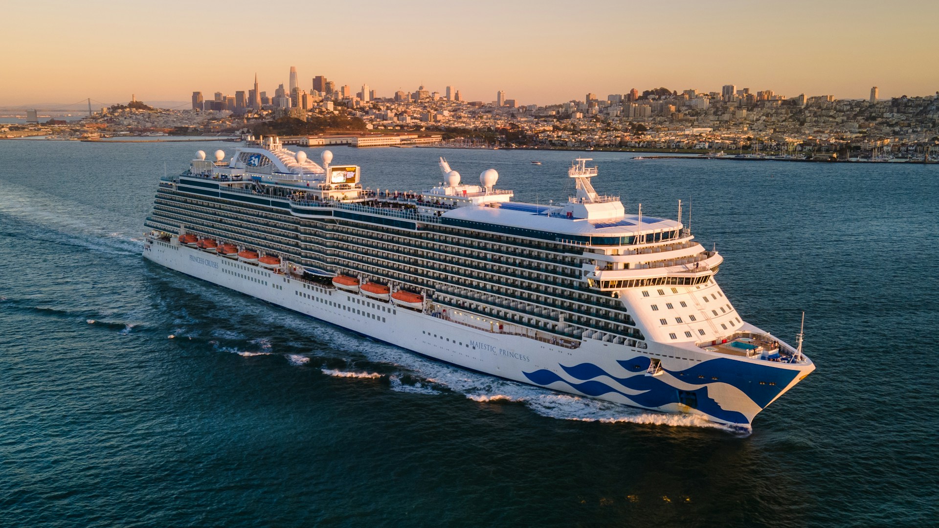 a large cruise ship in the ocean with a city in the background