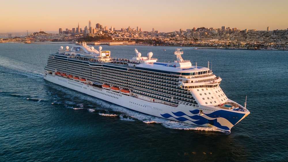 a large cruise ship in the ocean with a city in the background