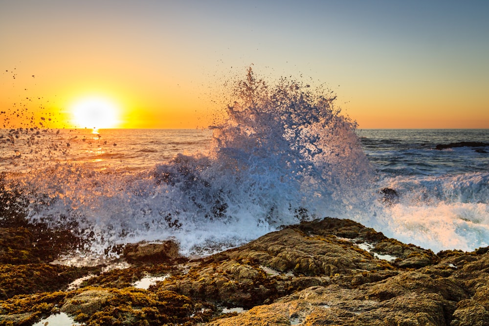 the sun is setting over the ocean with a crashing wave