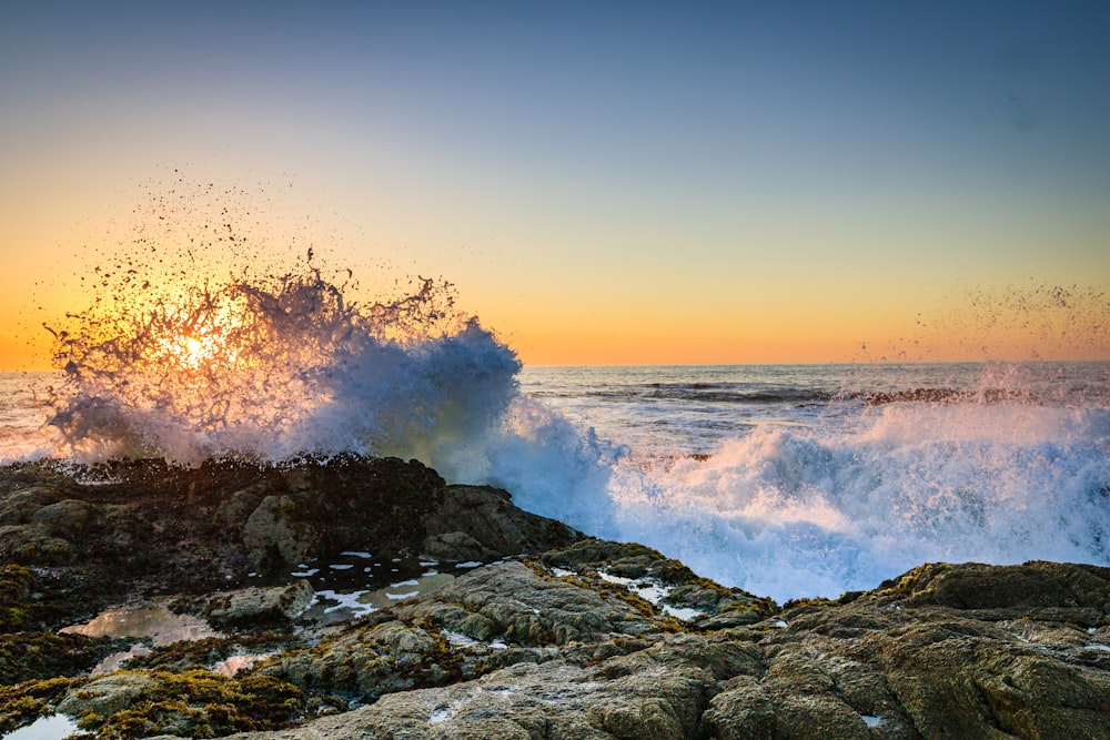 a wave crashes on a rocky shore as the sun sets