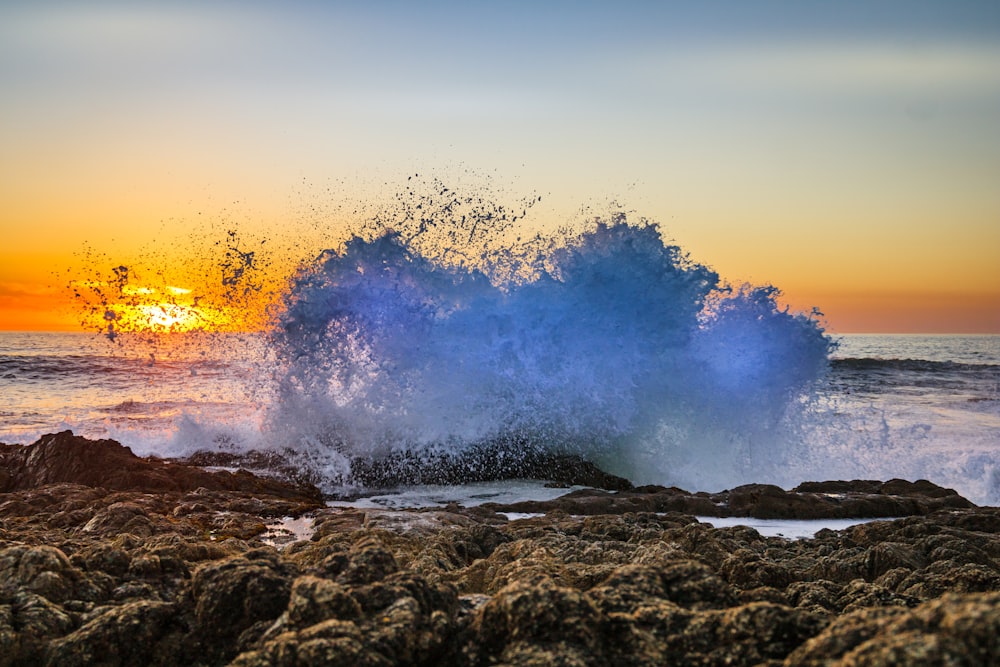 a wave crashing on a rocky shore at sunset