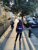 A bright morning street scene with children walking towards the school ride car.