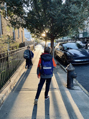 A bright morning street scene with children walking towards the school ride car.