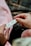 A person is holding a home pregnancy test with two visible lines, indicating a positive result. The background shows a soft and warm environment with a pink textured blanket and a plaid pattern fabric.