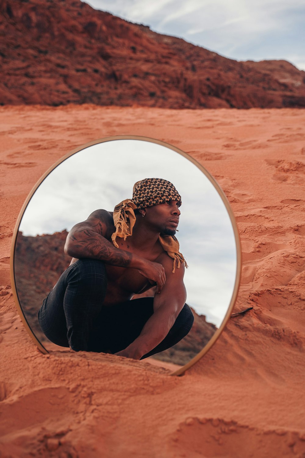 a man sitting in the sand in front of a mirror