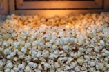 A pile of freshly popped popcorn fills the frame, with a warm, golden light illuminating the fluffy kernels. The texture of the popcorn is detailed, showcasing the irregular shapes and slightly crispy edges.