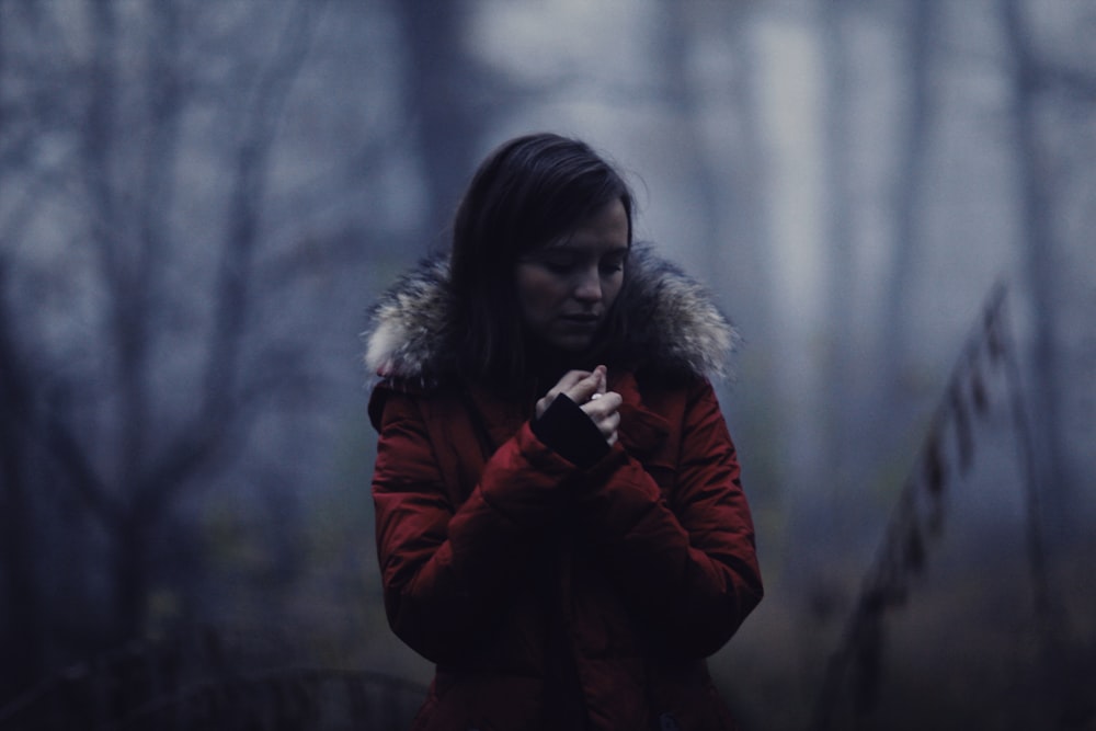 a woman in a red coat standing in a forest