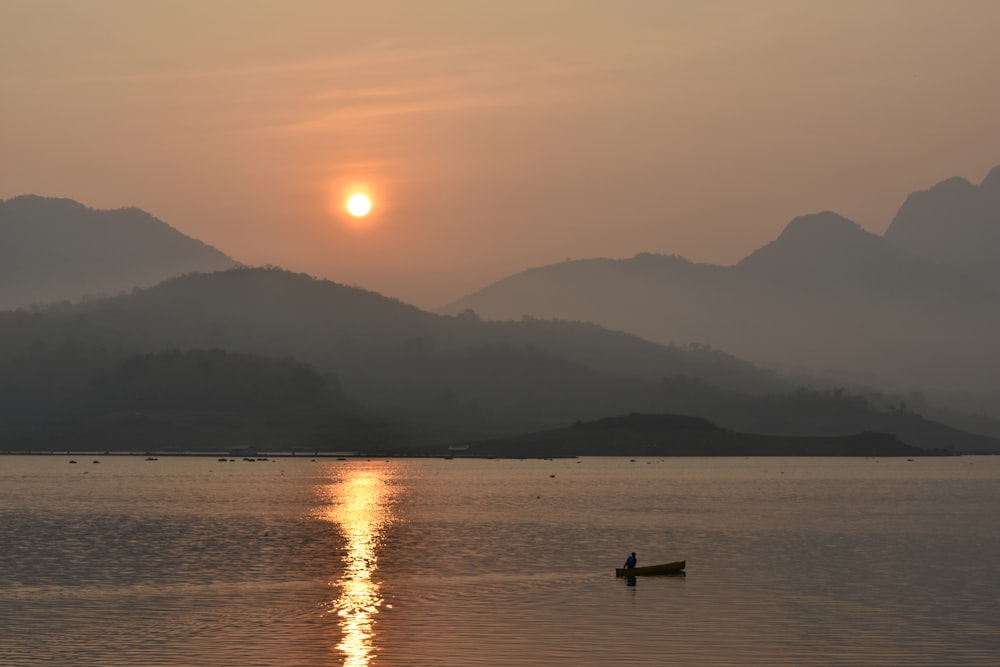 the sun is setting over a lake with mountains in the background