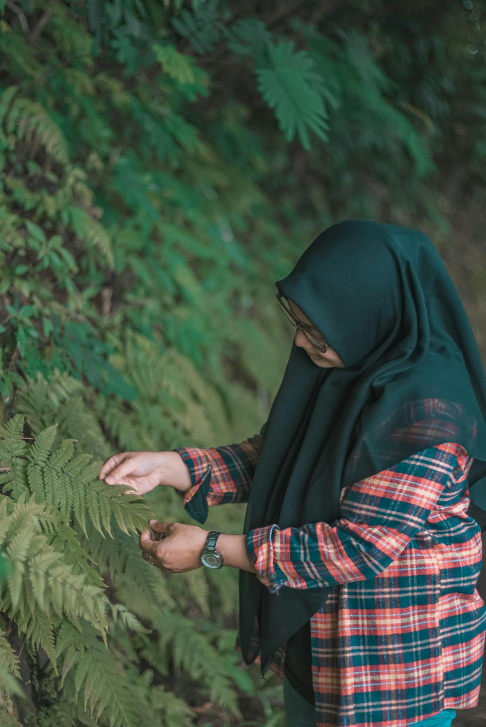 a woman in a hijab is picking leaves from a tree