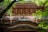 A traditional Japanese wooden structure with intricate architectural details is framed by vibrant green foliage. The building features layered eaves and carefully crafted wooden beams, showcasing the beauty and artistry of traditional design.