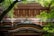 A traditional Japanese wooden structure with intricate architectural details is framed by vibrant green foliage. The building features layered eaves and carefully crafted wooden beams, showcasing the beauty and artistry of traditional design.