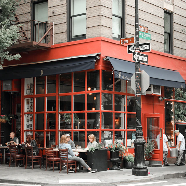 People sitting at sidewalk tables outside a corner restaurant on Bedford Street in New York