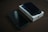A smartphone lies on top of its box on a dark surface, with another phone placed nearby. The box displays a logo, suggesting a brand. Both phones appear to have dark screens.