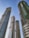 Four tall skyscrapers under construction rise against a clear blue sky. The buildings feature modern architectural designs with glass and concrete elements. Green safety nets are visible on some sections, indicating ongoing construction work.