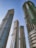Four tall skyscrapers under construction rise against a clear blue sky. The buildings feature modern architectural designs with glass and concrete elements. Green safety nets are visible on some sections, indicating ongoing construction work.