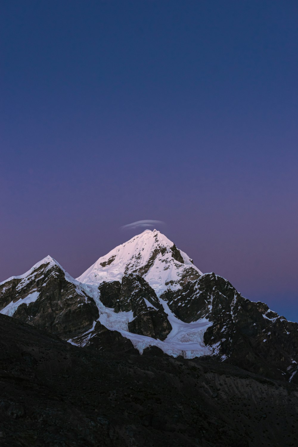 the top of a snow covered mountain under a purple sky