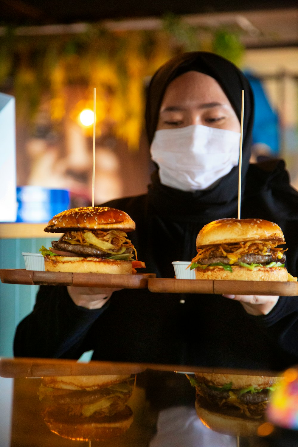 a woman wearing a face mask holding a tray of sandwiches