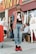 A person stands confidently in front of a vintage clothing store, wearing a plaid shirt over a graphic tee, jeans, and red sneakers. Several other individuals are in the background, some interacting and others casually pose. The storefront displays vibrant signage and mannequins wearing vintage-style outfits.