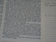A close-up of a book or bible page showing printed text on the left side. The text is about a religious or historical topic, mentioning leaders and events. Handwritten notes can be seen on the lined section to the right, indicating engagement with the text.