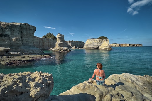 a woman sitting on a rock near the ocean