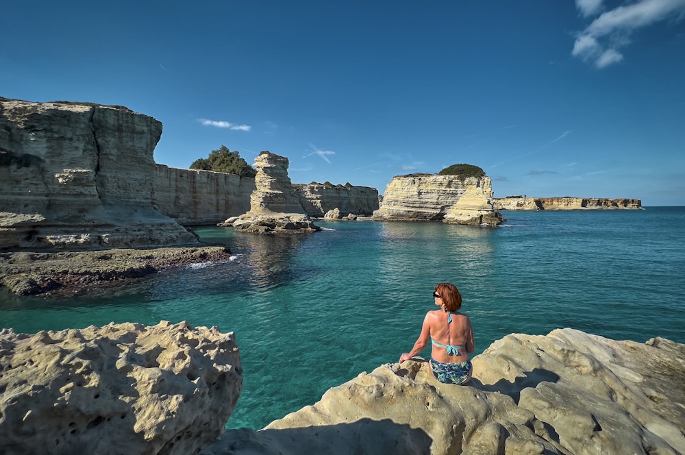 a woman sitting on a rock near the ocean