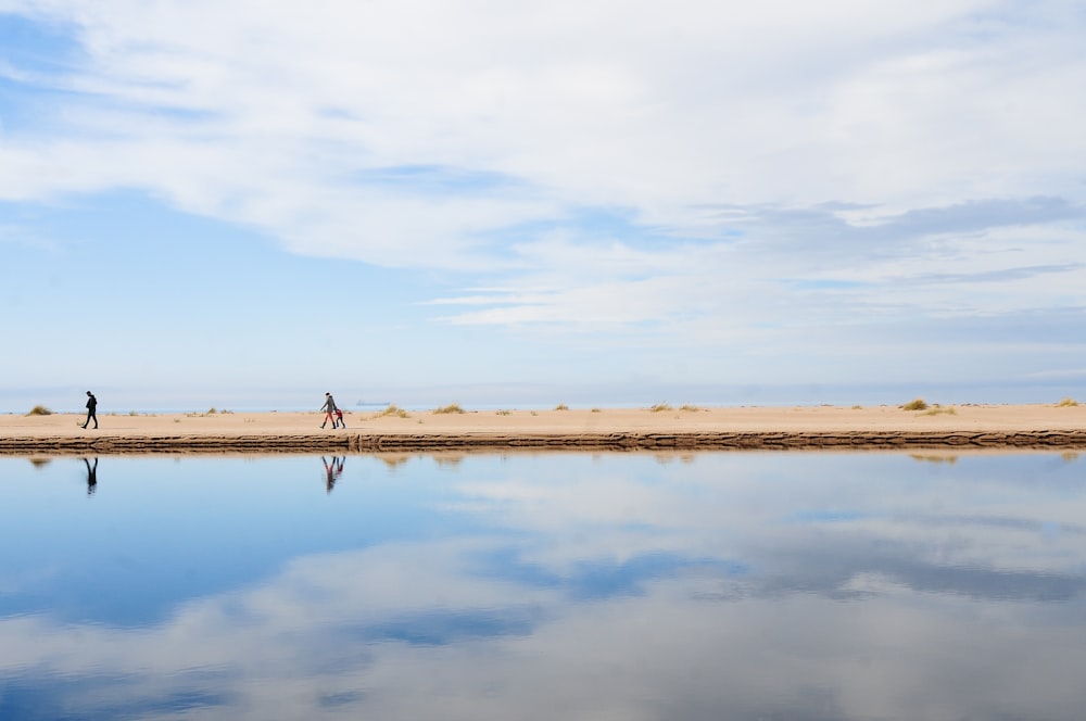 Due persone che camminano su una spiaggia vicino a uno specchio d'acqua
