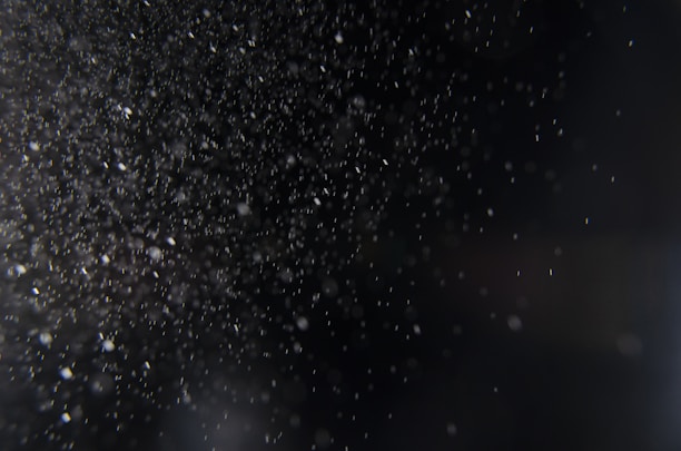A multitude of small particles or dust is suspended in the air against a dark background, creating a sense of depth and texture.