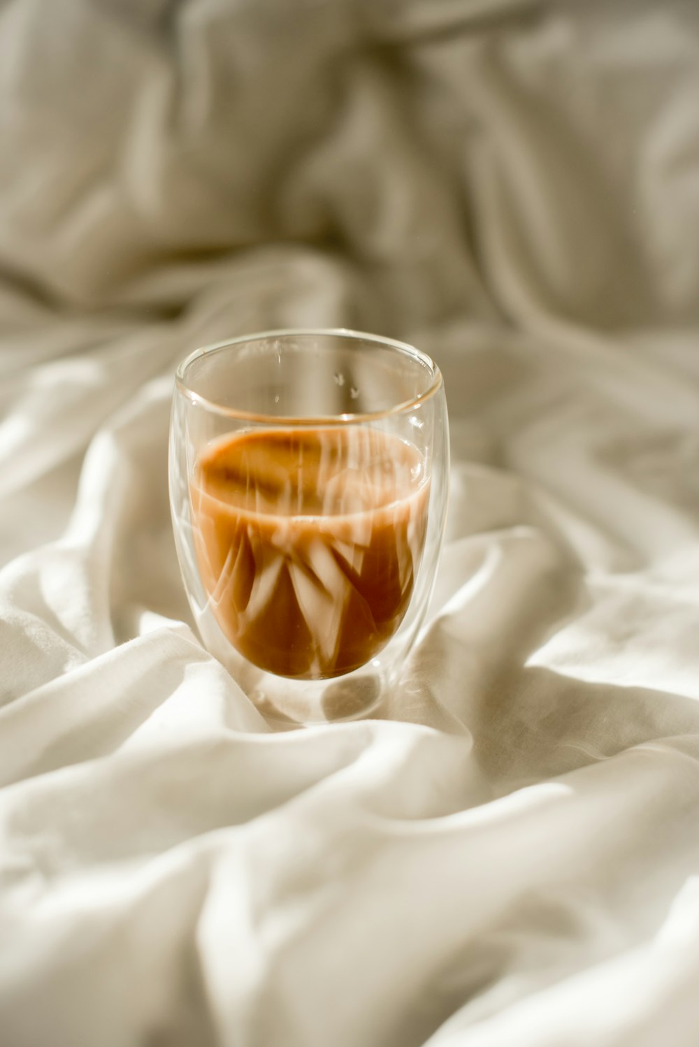a glass filled with liquid sitting on top of a bed