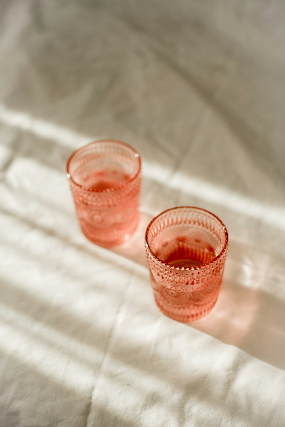 two pink glasses sitting on top of a white sheet