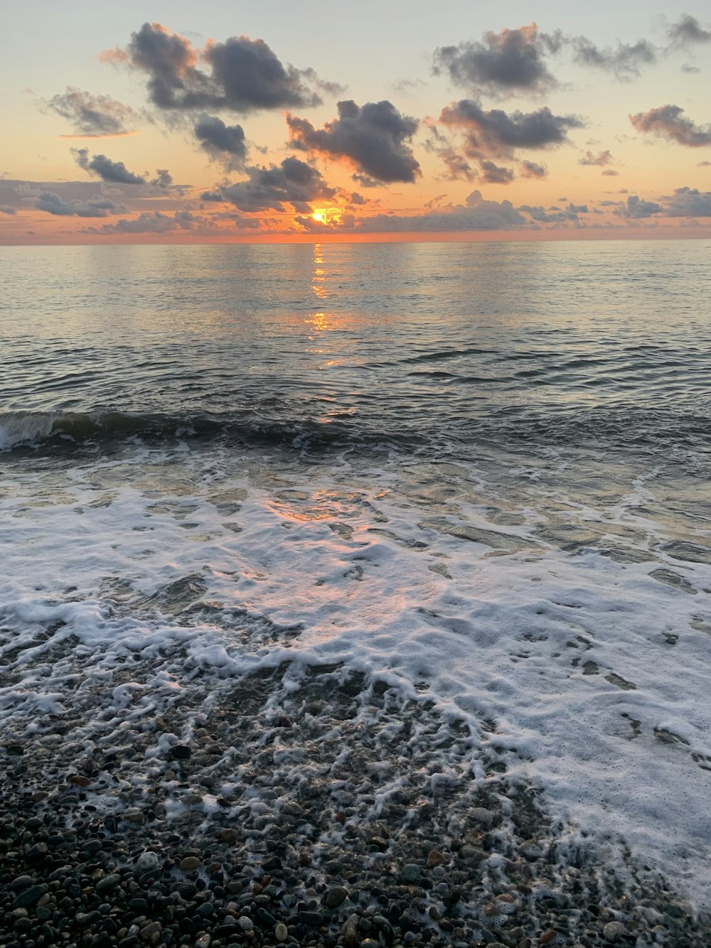 the sun is setting over the ocean on a cloudy day