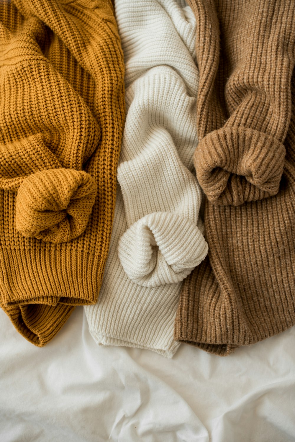 three different colors of sweaters laying on a bed