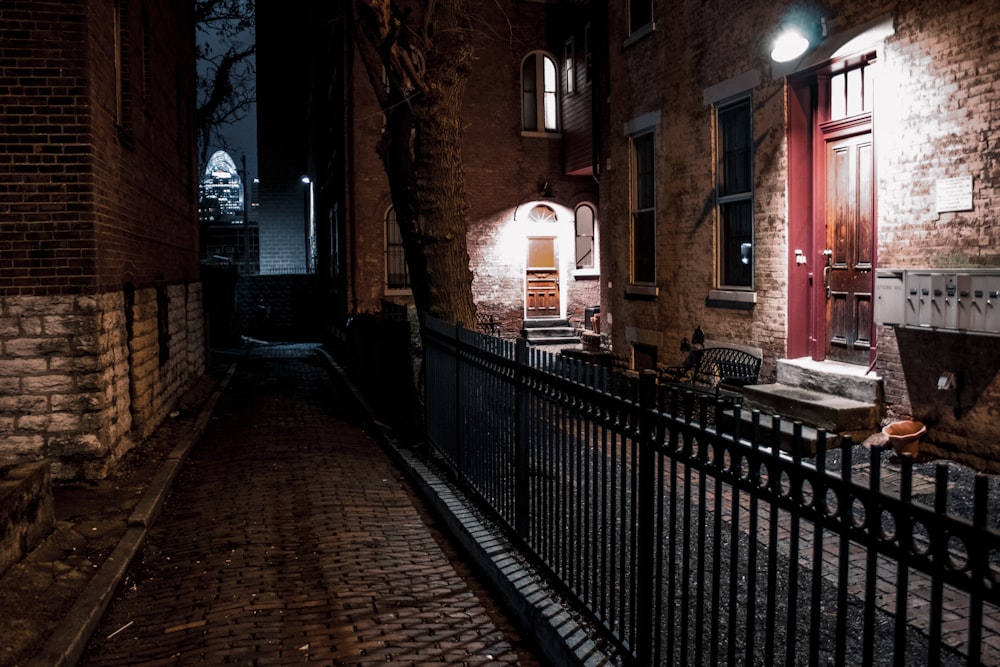 a dark alley at night with brick walls and a wrought iron fence