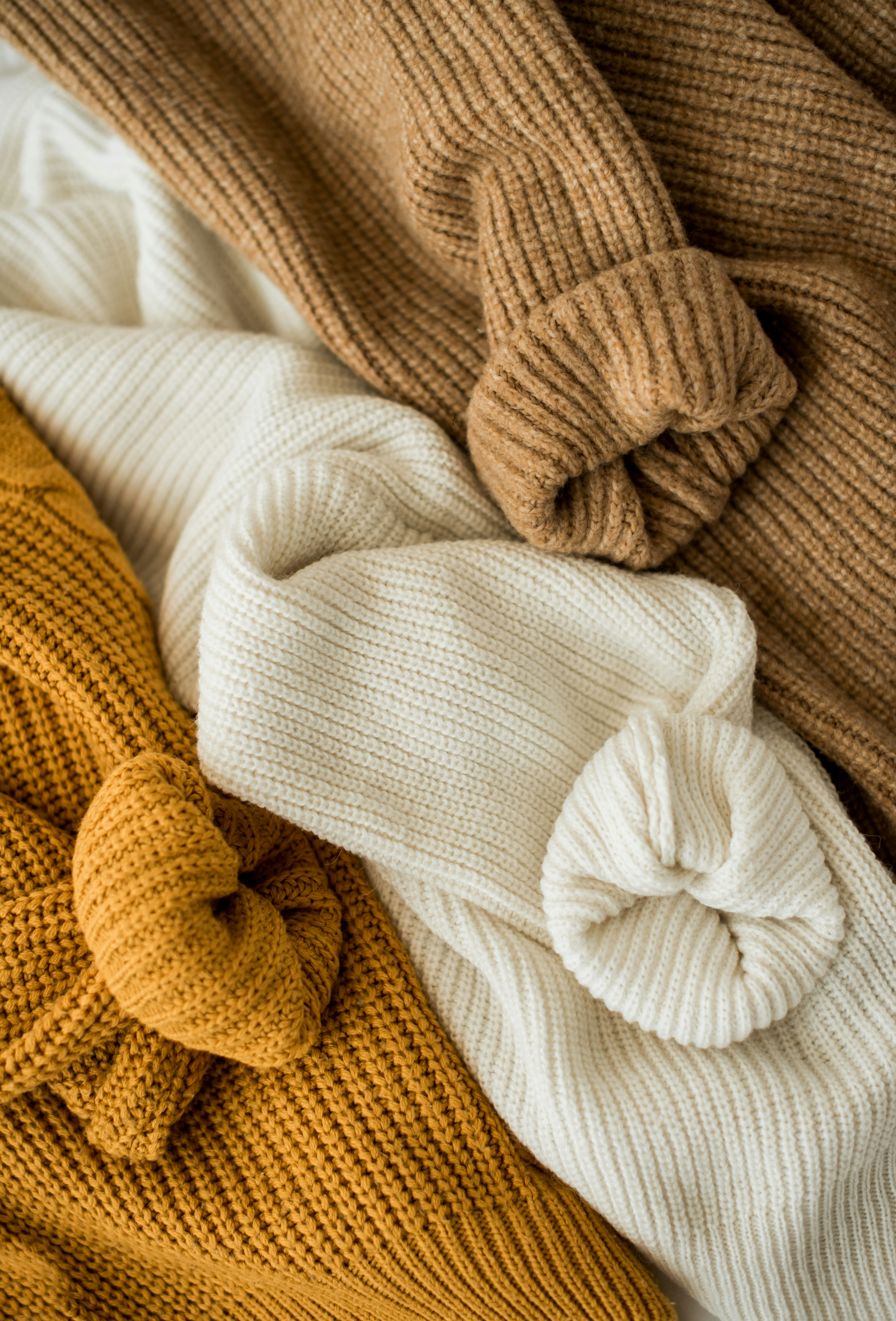 pile of cozy, chunky knit sweaters in brown, cream, and mustard