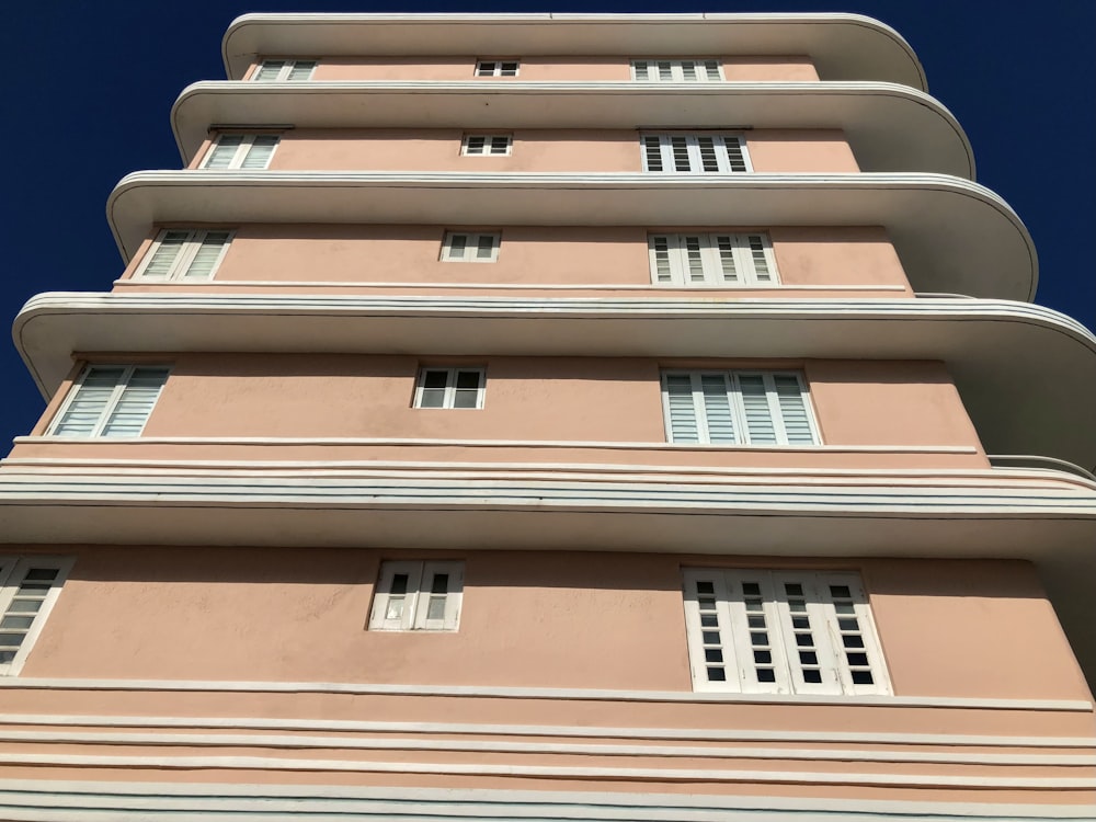 a tall pink building with white windows and shutters