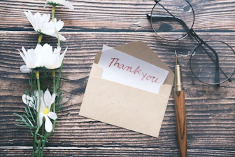 a thank you note sitting on top of a table next to a pair of glasses